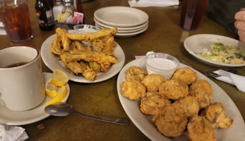 Two plates of fried food: one with chicken wings and dipping sauce, the other with fried biscuits, alongside a cup of tea.