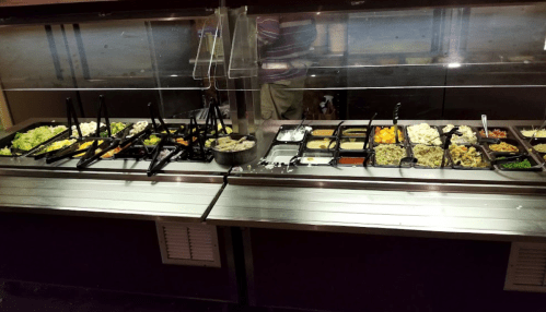 A buffet with various food items, including salads, vegetables, and proteins, displayed in black trays.