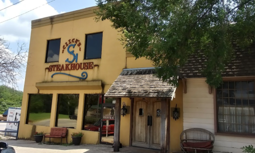 A yellow building with a sign reading "Steakhouse," featuring a wooden door and outdoor seating.