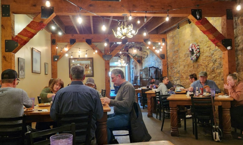 A cozy restaurant interior with wooden beams, string lights, and diners enjoying meals at wooden tables.
