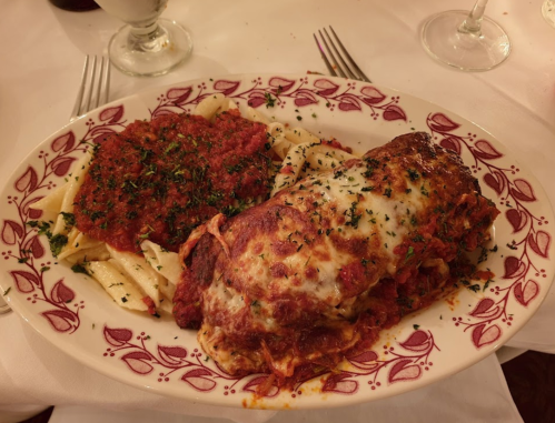 A plate of lasagna topped with marinara sauce and herbs, served alongside pasta with red sauce and parsley.