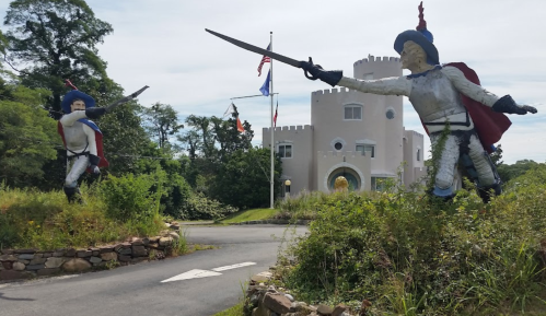 Two large knight statues with swords face each other at the entrance of a castle-like building surrounded by greenery.