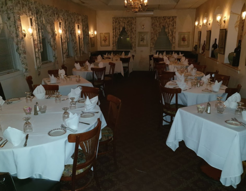 A dimly lit restaurant with neatly set tables, white tablecloths, and floral curtains, creating an elegant atmosphere.
