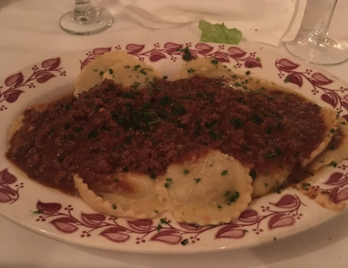 A plate of ravioli topped with a rich meat sauce and garnished with parsley.