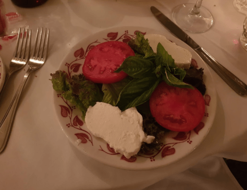 A plate of salad with mixed greens, sliced tomatoes, and dollops of fresh cheese, garnished with basil leaves.
