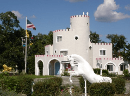 A whimsical white castle with red accents, featuring a unicorn statue and flags in the foreground.