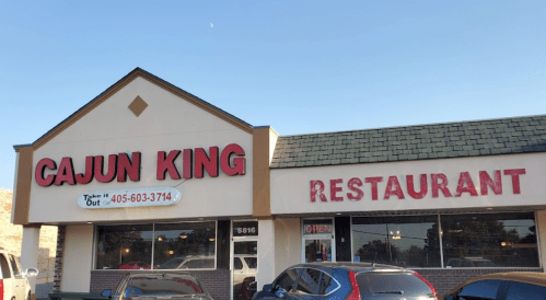 Exterior of Cajun King restaurant with a sign and open hours, featuring a clear blue sky and parked cars.