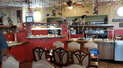 A colorful restaurant interior with decorated walls, empty tables, and a buffet area in the background.