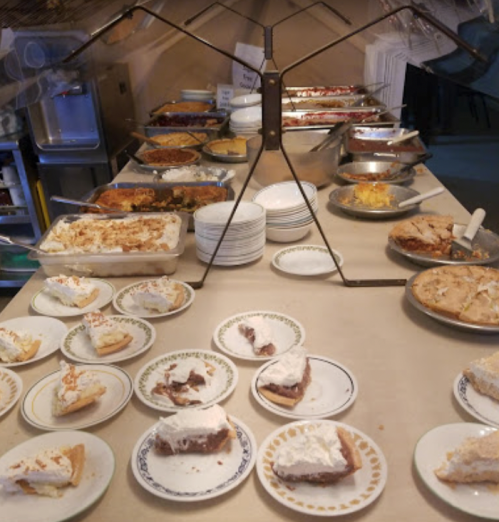 A dessert table featuring various pies and cakes, with plates of sliced desserts in the foreground.