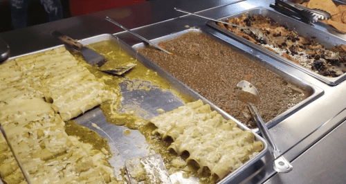 A metal tray with green enchiladas, a side of lentils, and a dish of baked goods.