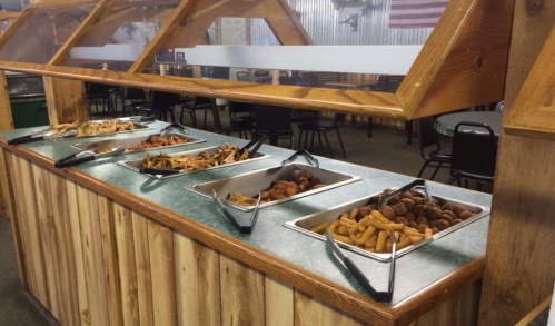 A buffet station with various trays of food, including meats and appetizers, in a rustic dining setting.