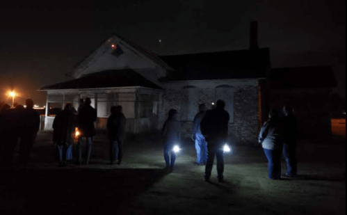 A group of people with flashlights exploring an old, dimly lit house at night.