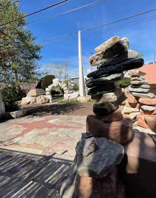 A stack of rocks stands in a garden with stone pathways and greenery under a clear blue sky.
