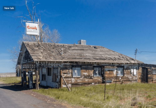 Abandoned wooden building with a weathered exterior and a sign, set against a clear blue sky.