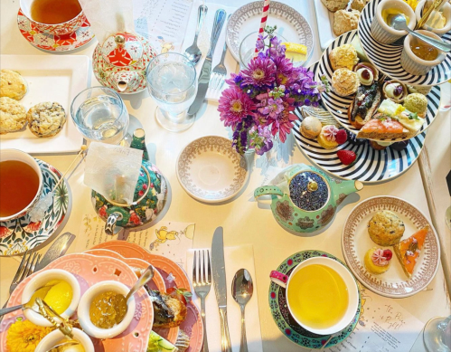 A beautifully arranged table with various teas, pastries, and a floral centerpiece, showcasing an elegant afternoon tea setting.