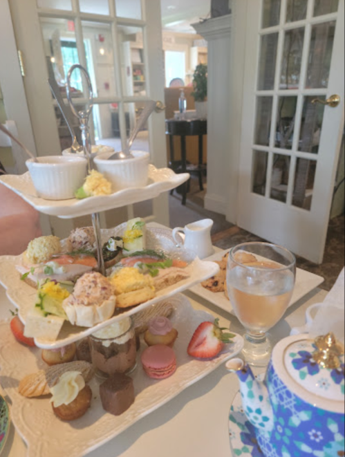 A tiered stand of assorted pastries and finger foods, with a glass of drink and a teapot on a table.
