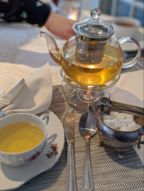 A teapot with brewed tea sits on a table beside a cup, spoon, and a sugar bowl with sugar cubes.