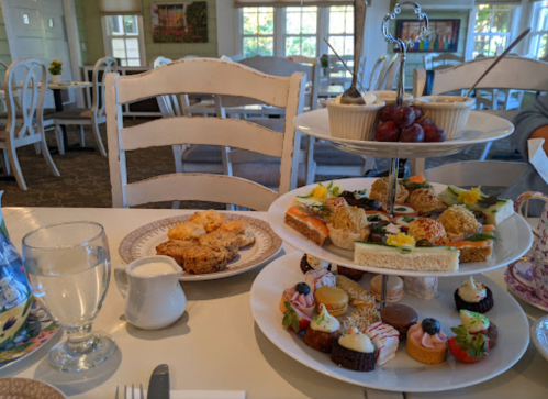 A tiered stand with assorted pastries and sandwiches, alongside a plate of scones and a glass of water on a table.