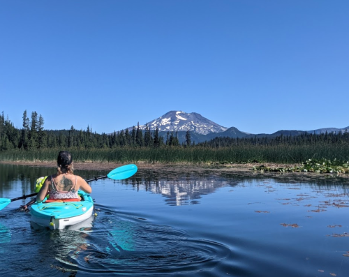 A person kayaking on a calm lake with a mountain in the background under a clear blue sky.