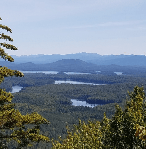 A scenic view of mountains and lakes surrounded by lush greenery under a clear blue sky.