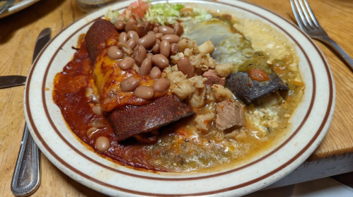 A plate of enchiladas topped with beans, meat, and a side of green and red sauces, garnished with lettuce.