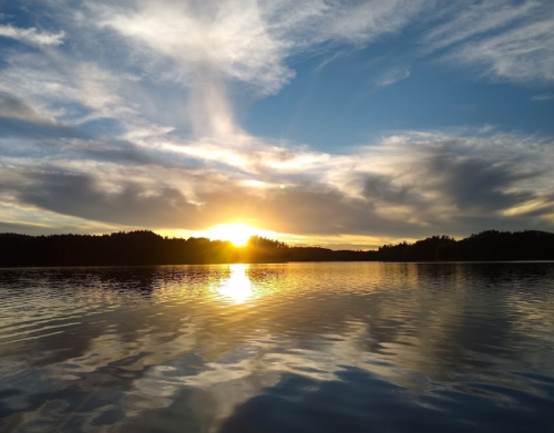 A serene sunset over a calm lake, with vibrant clouds reflecting on the water's surface.