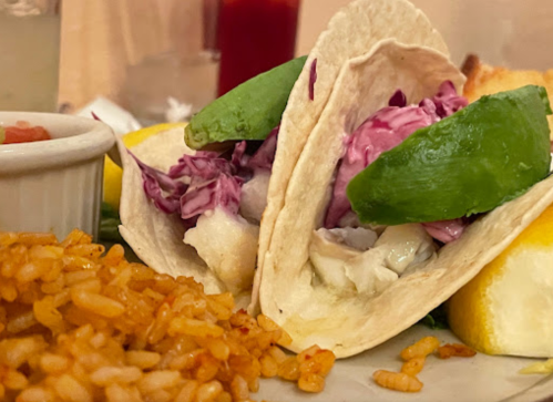 Two fish tacos with cabbage and avocado, served with lemon and a side of rice.