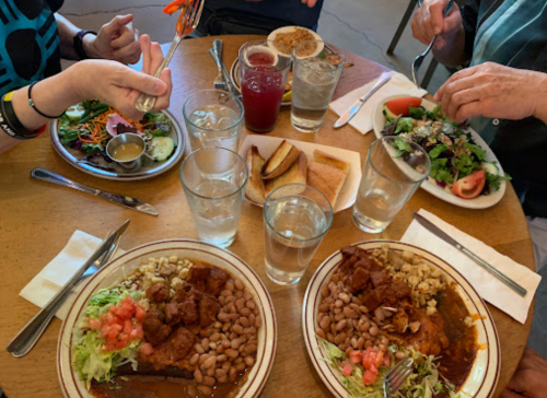 A table with two plates of food featuring rice, beans, and salad, surrounded by drinks and additional dishes.
