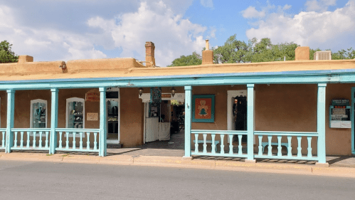 A colorful adobe-style building with a blue porch, featuring shops and a clear sky in the background.
