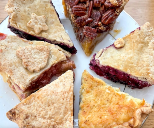 A plate with six slices of various pies, including fruit and pecan, decorated with small pastry shapes.