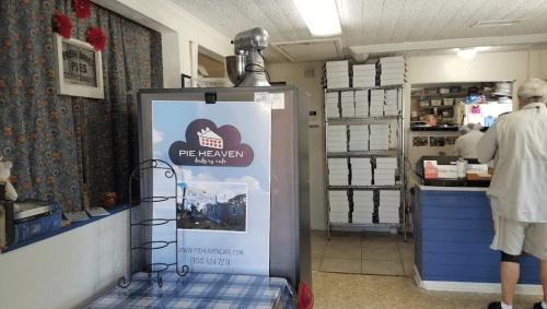 Interior of a pie shop with a display fridge, stacked boxes, and a customer at the counter. Cozy atmosphere.