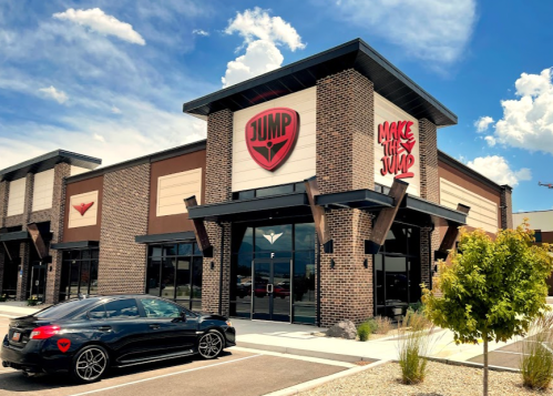 A modern building with a large "JUMP" sign, featuring a sleek car parked in front and a clear blue sky above.