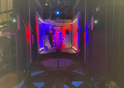 A futuristic room with colorful lights, featuring two figures walking through a high-tech environment.