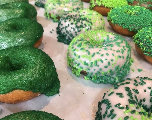A variety of green donuts topped with sprinkles, arranged on a white surface.