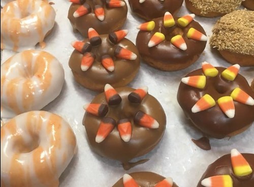 A variety of decorated donuts, including chocolate and glazed, topped with candy corn and other festive designs.