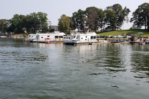 A calm marina with several boats docked, surrounded by trees and a grassy area under a clear sky.
