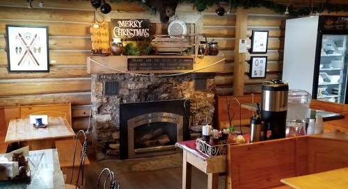Cozy restaurant interior with a stone fireplace, Christmas decorations, and wooden tables.