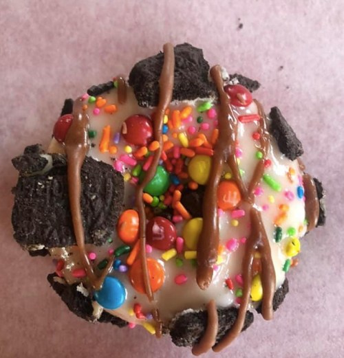 A colorful donut topped with icing, sprinkles, chocolate drizzle, and crushed cookies.