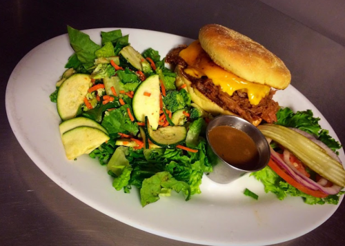 A plate featuring a cheeseburger with lettuce, a side salad, and a small cup of dressing.