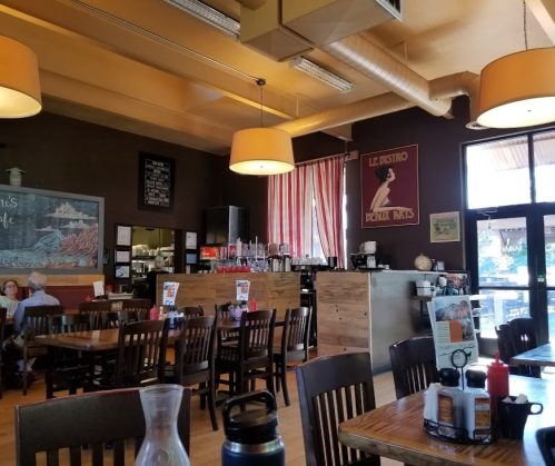 Cozy restaurant interior with wooden tables, chairs, and a chalkboard menu, featuring warm lighting and decorative posters.