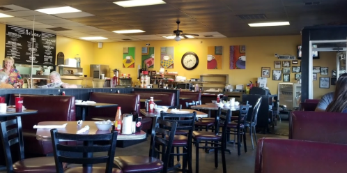 A cozy diner interior with empty tables, colorful wall art, and a clock, featuring ketchup and mustard on the tables.