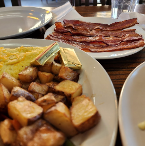 A plate with an omelet, crispy bacon, and golden-brown roasted potatoes, set on a wooden table.