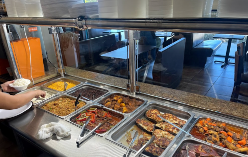 A buffet with various dishes, including rice, beans, and vegetables, with a person serving food in the foreground.