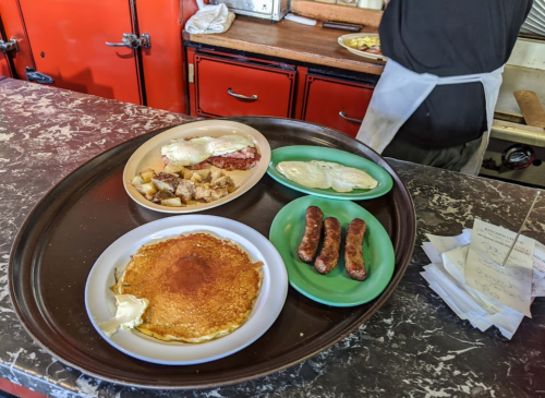 A tray with pancakes, sausages, eggs, and hash browns in a diner setting.