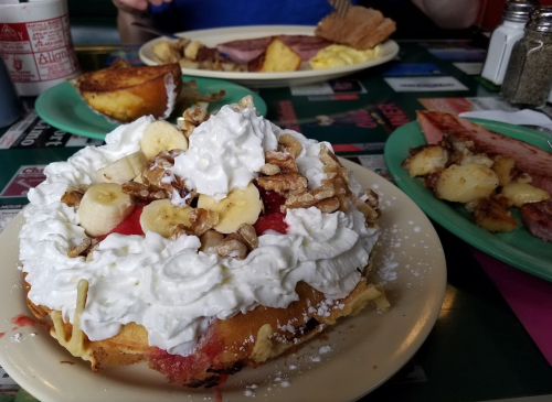 A dessert plate featuring a large, whipped cream-topped cake with bananas and walnuts, alongside a breakfast spread.