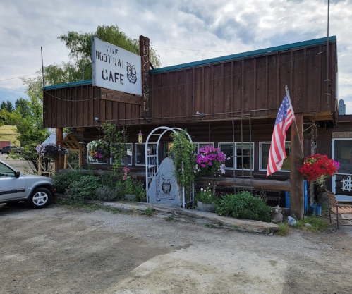 A rustic café with a wooden exterior, colorful flowers, and an American flag in front.