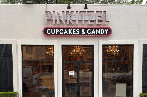 Exterior of Pinkitzel Cupcakes & Candy shop, featuring a bright sign and large windows.