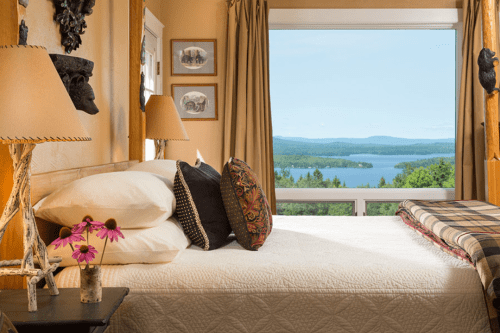 Cozy bedroom with a lake view, featuring a bed with decorative pillows and a vase of flowers on the nightstand.
