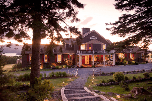 A charming house at sunset, surrounded by trees and a landscaped garden, with a welcoming porch and pathway.