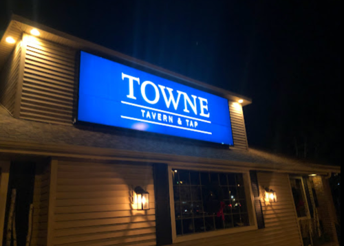 A brightly lit sign reading "TOWNE TAVERN & TAP" on a building exterior at night.